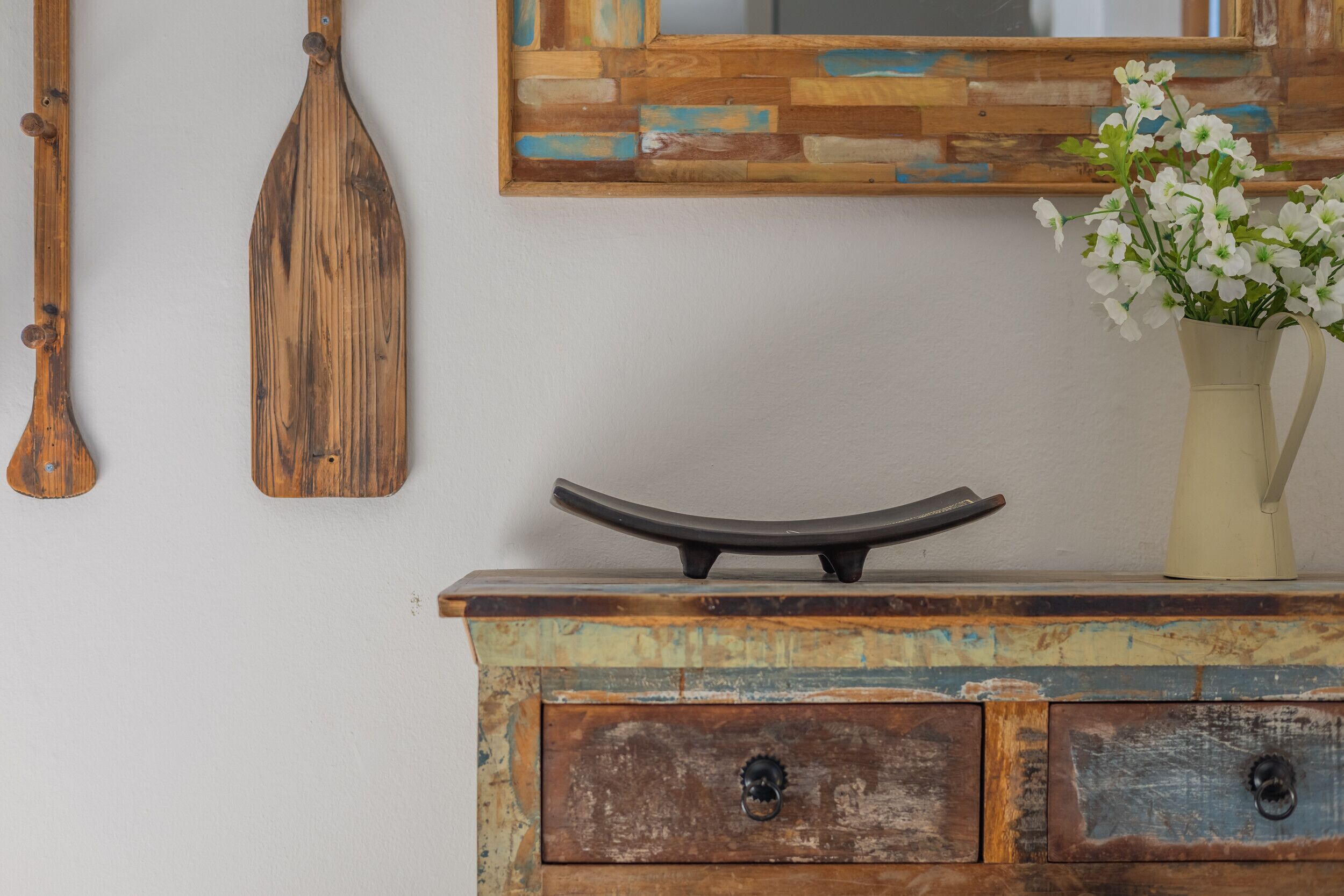 A rustic wooden dresser with drawers, a mirror with a wooden frame, and a vase with flowers.