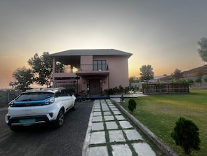 A two-story house with a driveway, a car parked in front, and a small garden. - Retreat at 3BHK Pool farmhouse near Ghrishneshwar Temple/Ajanta Ellora with AC (Chhatrapati sambhajinagar)