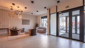 Una hall moderna di un hotel con una reception, un'area salotto e ampie porte vetrate che danno sull'esterno.