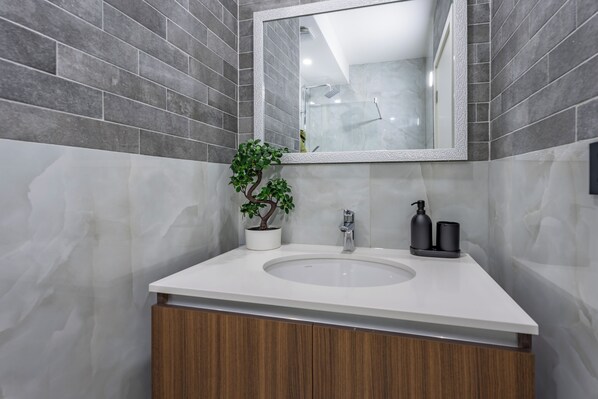 A bathroom with a white sink, a mirror, a potted plant, and a shower area. - Hotel Eterna Hill Rooftop (Belgrade)