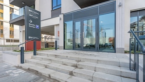 Ingresso moderno di un edificio con una scala che conduce a una porta in vetro, un cartello che indica un garage e il riflesso di un grattacielo nel vetro.
