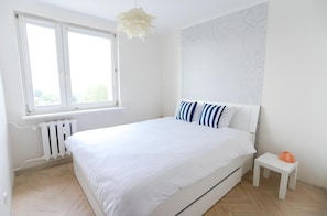 A bedroom with a bed, a radiator, a window, and a small table with an orange object. - Domki Całoroczne Jaga (Olsztyn)