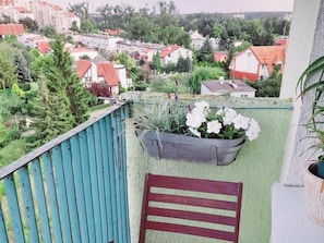 A balcony with a view of a residential area, a potted plant with white flowers, and a wooden chair. - Domki Całoroczne Jaga (Olsztyn)