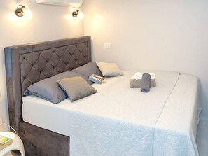 Ein ordentlich bezogenes Bett mit einer gepolsterten Kopfstütze, Kissen, einem aufgerollten Handtuch und einem Buch auf dem Bett.