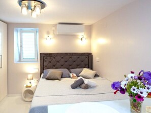 Ein Schlafzimmer mit einem Bett, Nachttischlampen, einem Fenster, einer Klimaanlage und einer Vase mit Blumen.