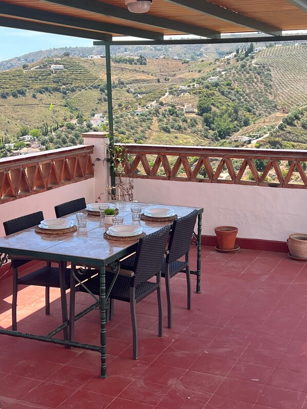 Um terraço com mesa posta para refeições, com vista para uma paisagem montanhosa.