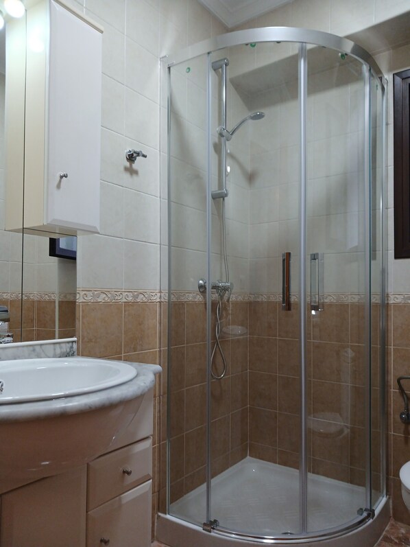 Un baño con ducha acristalada, un lavabo y un armario.