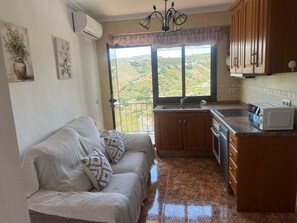 A kitchen with a sofa, a window with a view, and a microwave.