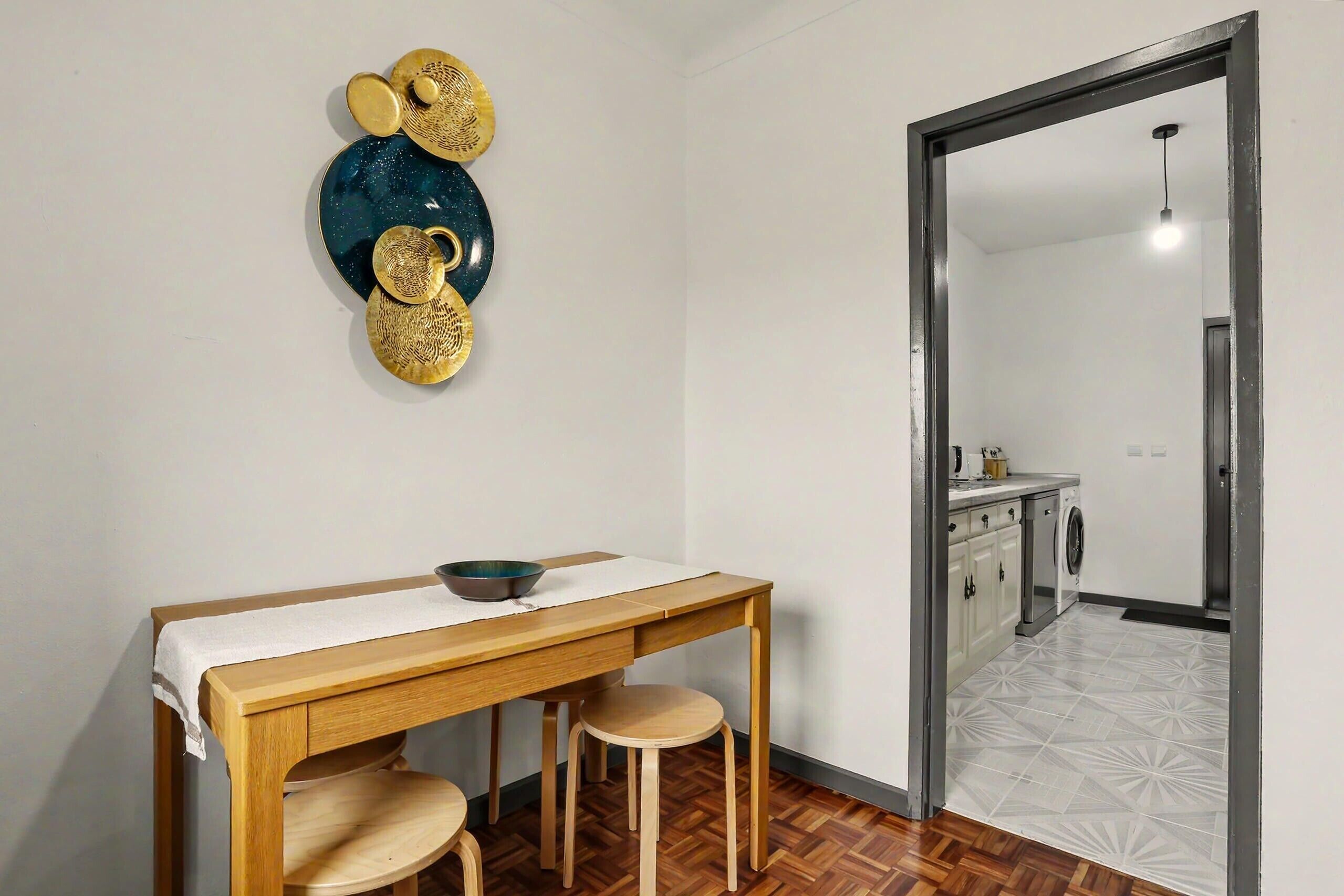 A dining area with a wooden table, two stools, and a decorative wall piece.