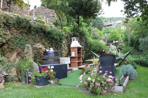 Un jardín con un muro de piedra, una parrilla de ladrillo y una hamaca.