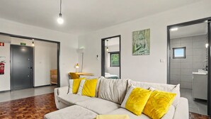 A modern hotel room with a sofa, a small table, a mirror, and a door leading to a bathroom. - Cantinho do Préstimo (Préstimo)