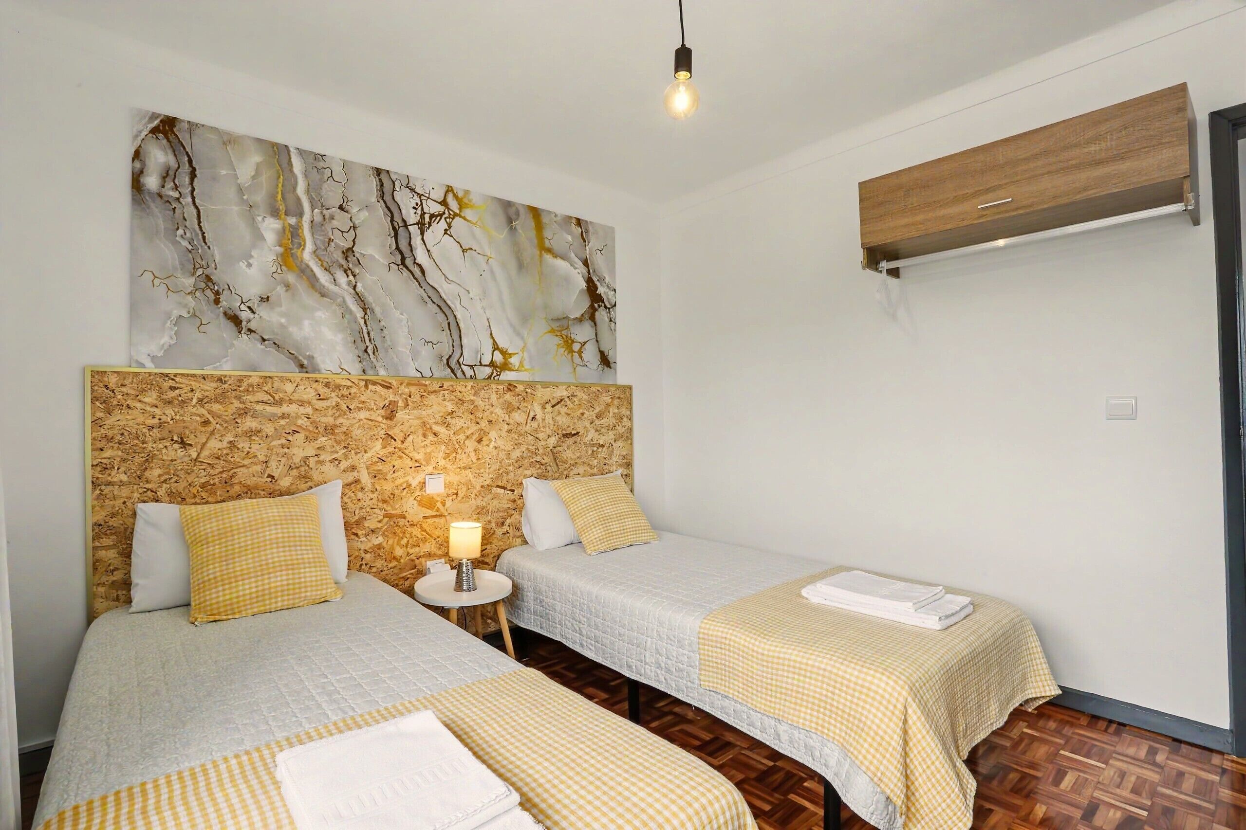 Habitación de hotel con dos camas, una obra de arte en una pared de mármol, un cabecero de madera, una mesita de noche con lámpara y un equipo de aire acondicionado.