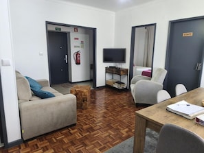 Una habitación amoblada con sofá, sillón, mesa, televisión y extintor.