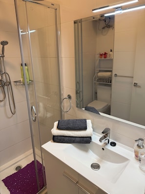 A modern bathroom with a glass-enclosed shower, a white sink, and a mirror.