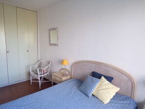 A bedroom with a bed, a chair, a nightstand, a lamp, and a wardrobe. - 3-room apt with pool, near beach, wifi, parking - great for families (La Grande-Motte)