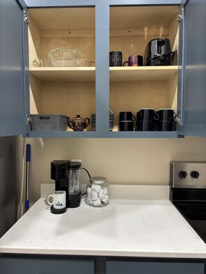 Una cocina con cafetera, hervidor, taza y un tarro de vidrio sobre la encimera.