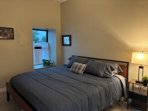 A bedroom with a bed, a bedside table with a lamp, a window with a view, and a plant. - Brand X Loft Spacious 2 Bedroom Loft in the Heart of Hebron (Hebron)