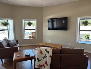 A living room with a brown couch, a wooden coffee table, a flat-screen TV mounted on the wall, and two windows with hanging plants. - Brand X Loft Spacious 2 Bedroom Loft in the Heart of Hebron (Hebron)