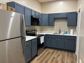 Una cocina con armarios azul oscuro, electrodomésticos de acero inoxidable y suelo de madera.