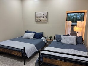 Un dormitorio con dos camas, un cuadro, una ventana con cortinas y una lámpara.