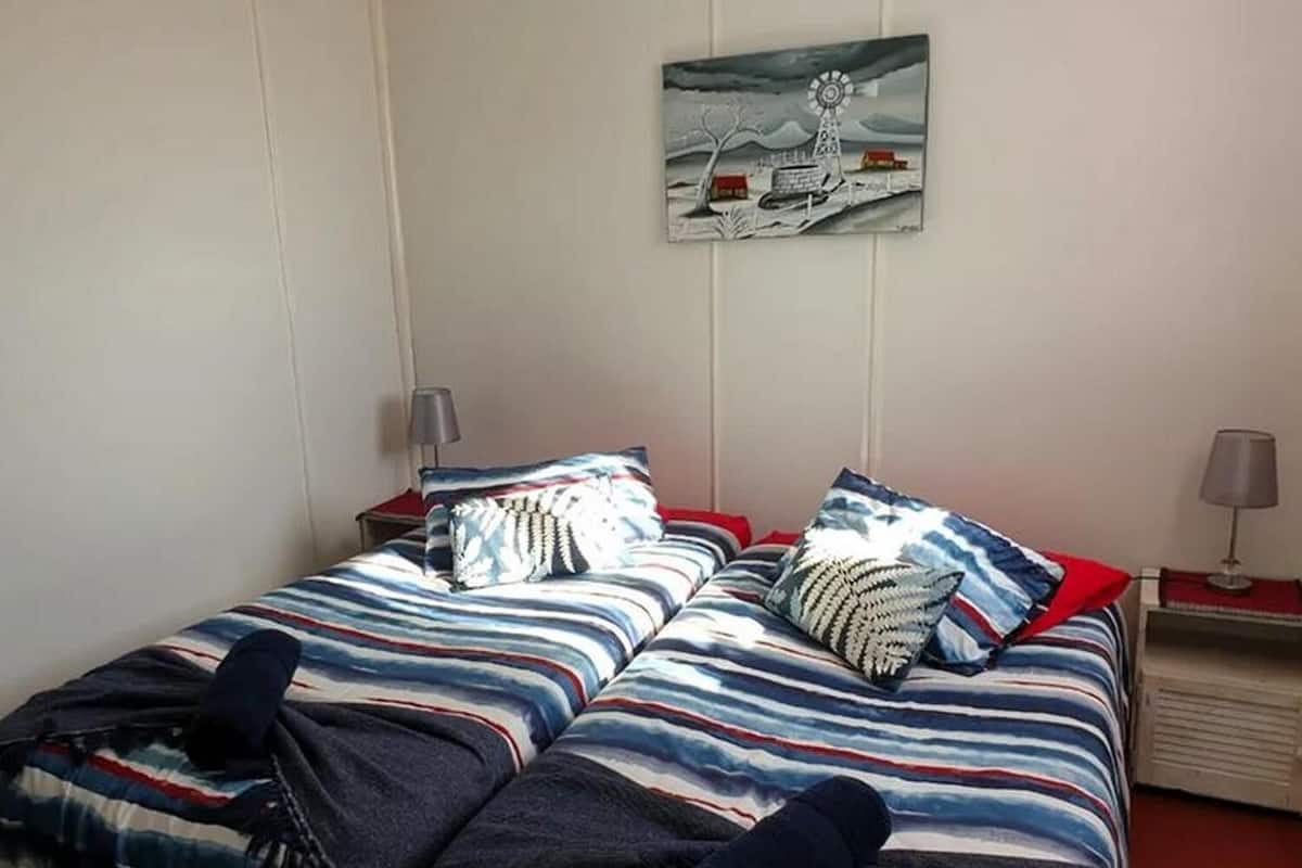 Una cama doble con ropa de cama a rayas, dos mesitas de noche con lámparas y un cuadro colgado en la pared de un molino.
