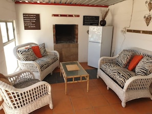 A room with wicker furniture, a glass-top table, a fireplace, and a refrigerator. - Honne-Pondokkies (Hondeklip Bay)