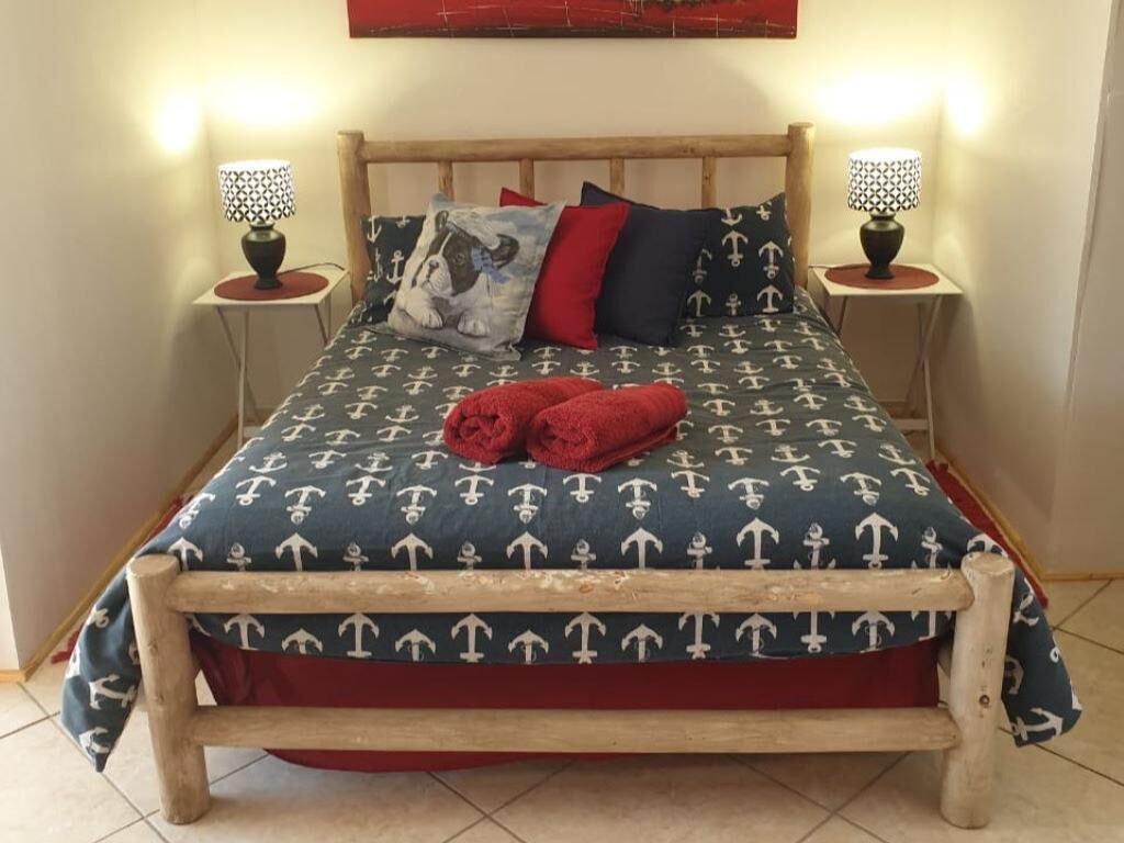 Een bed met een marine-thema beddegoed, twee bedlampen en een rode plaid.
