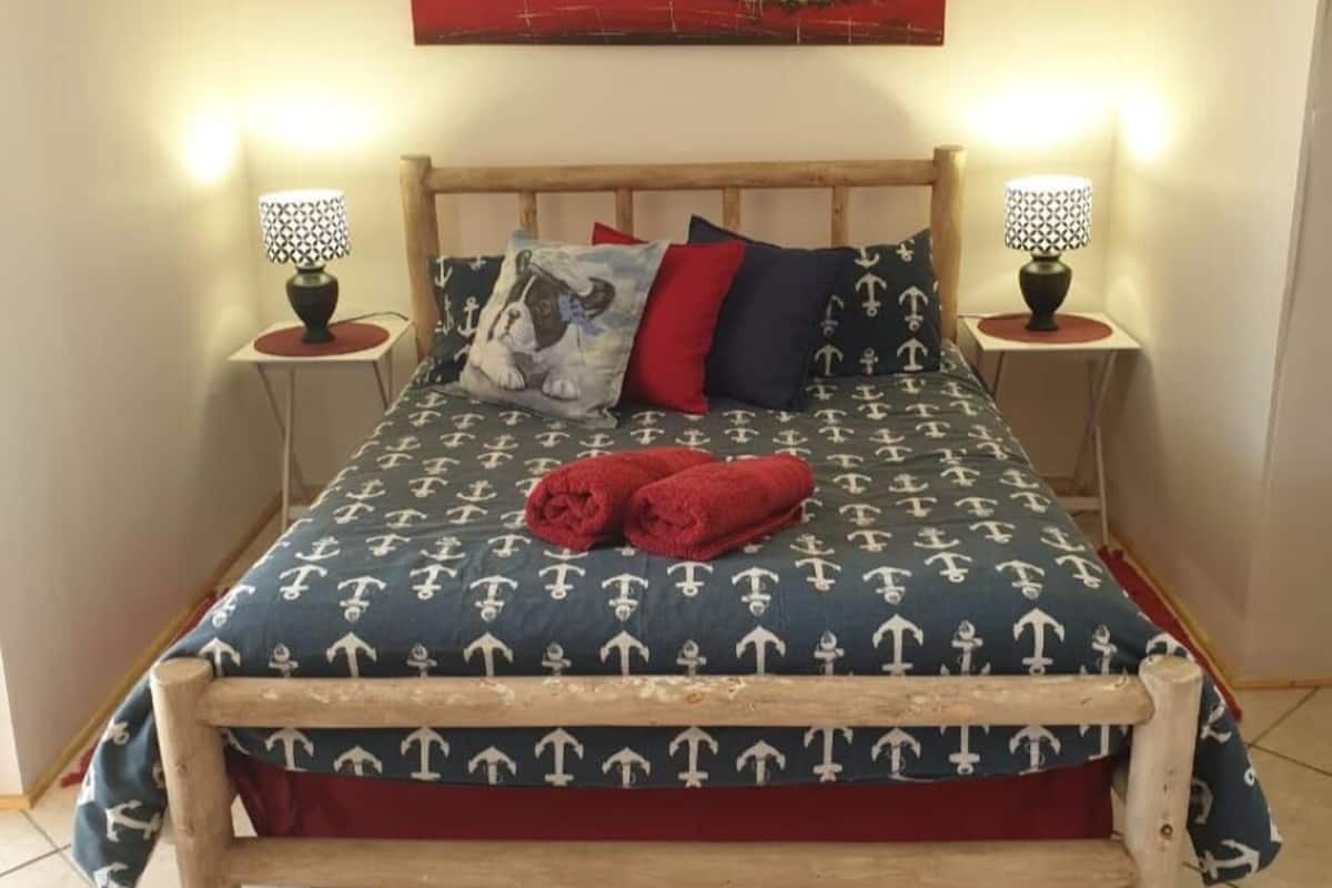 Una cama con una colcha de temática náutica, dos lámparas de noche y una manta roja.