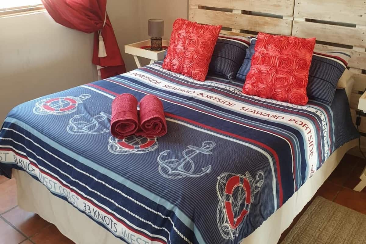 Una cama con una manta a rayas, almohadas rojas y toallas enrolladas.
