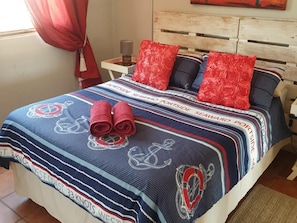 A bed with a striped blanket, red pillows, and rolled towels. - Honne-Pondokkies (Hondeklip Bay)