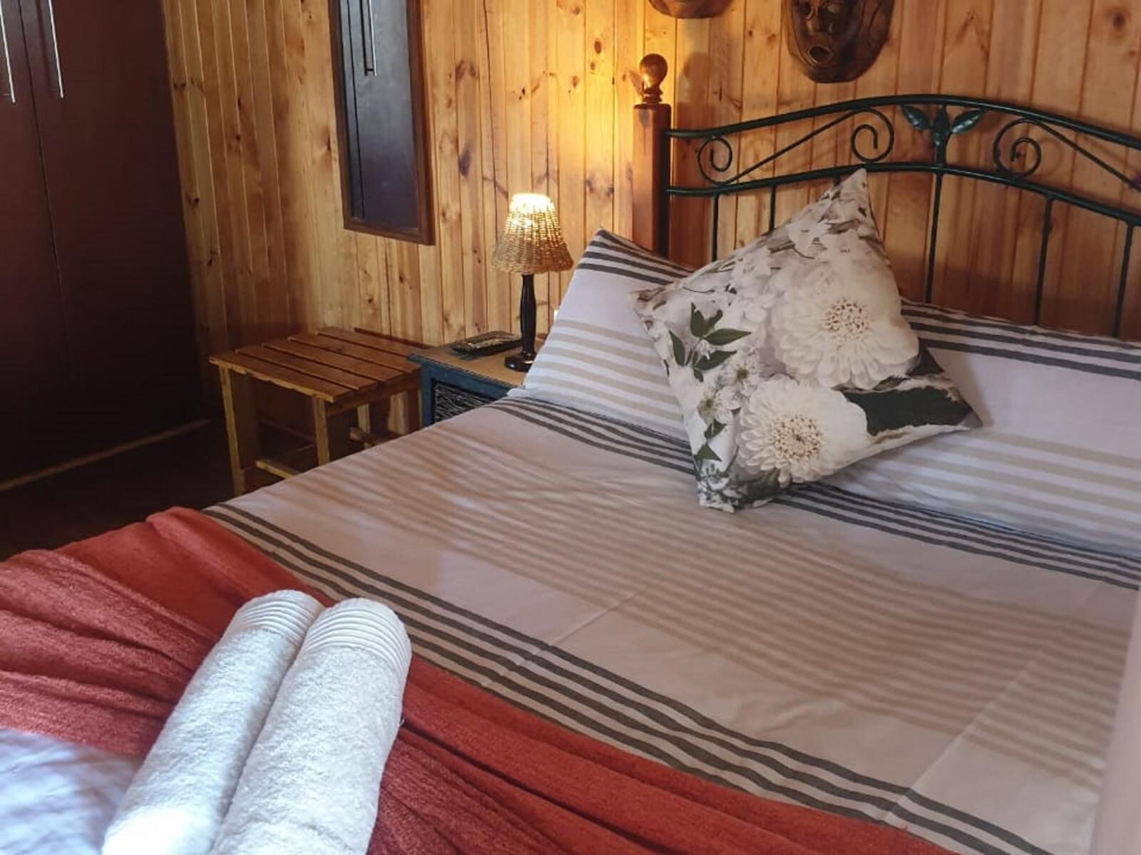 Een kamer met houten lambrisering, een bed, een nachtkastje, een lamp en een klein houten krukje.