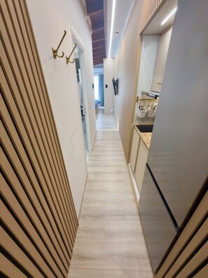 A narrow hallway with a wooden floor, a kitchen area with a refrigerator, and a bed in the background. - Apartment Vagia Nea Smyrni (Nea Smirni)