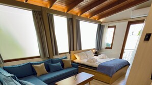 Ein modernes Zimmer mit einer Couch, einem Bett, Holzboden und großen Fenstern.