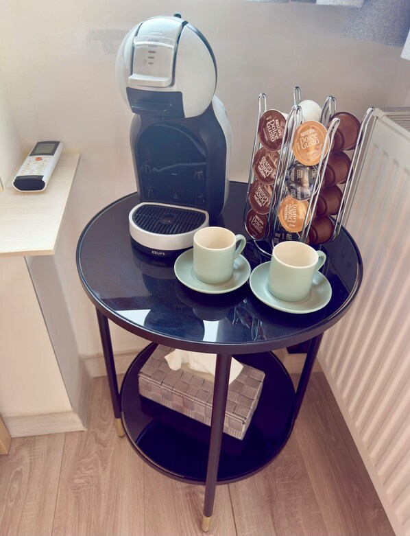 Uma pequena mesa com uma cafeteira, duas xícaras e um suporte para cápsulas de café.