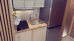 Eine kleine Küche mit Spüle, einem Edelstahl-Kühlschrank und hellen Schränken.