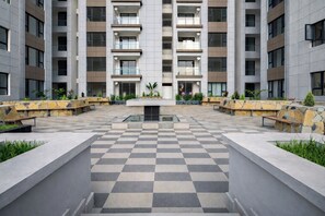 Un edificio moderno de varios pisos con un patio central que presenta un diseño de piso a cuadros, rodeado de bancos de piedra y jardineras.