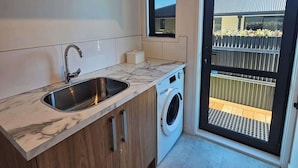 Eine kompakte Küche mit Spüle, Holzschränken, einer Waschmaschine und einer Glastür zum Balkon.