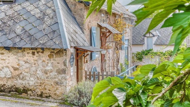 A stone building with a sloped roof, wooden shutters, and a small porch.