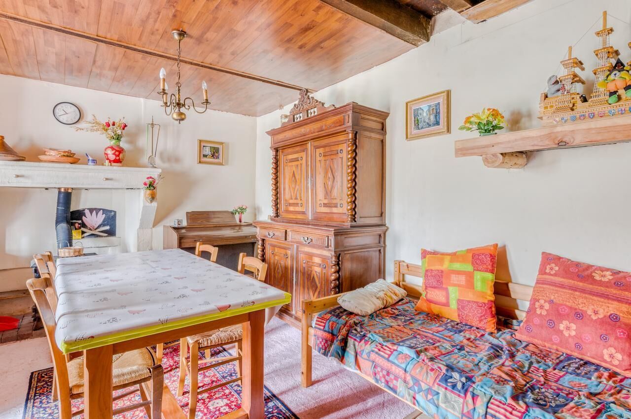 Une pièce chaleureuse avec un plafond en bois, une table à manger, un lit avec une literie colorée, une armoire en bois et une étagère ornée d’objets décoratifs.