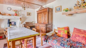 A cozy room with a wooden ceiling, a dining table, a bed with colorful bedding, a wooden cabinet, and a shelf with decorative items.