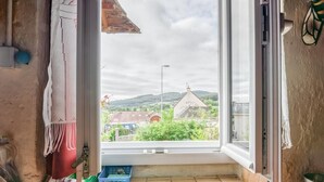A room with a large window, a view of a green landscape, a blue crate, and a metal sink.