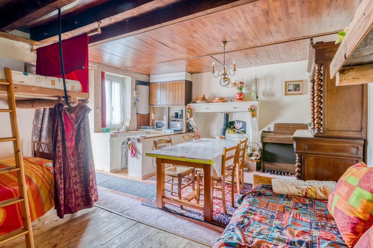 Une pièce confortable avec un lit superposé, une table à manger en bois avec des chaises, un petit coin cuisine et une commode en bois.