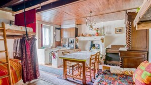 A cozy room with a bunk bed, a wooden dining table with chairs, a small kitchen area, and a wooden dresser.