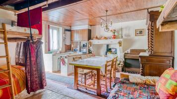 Une pièce confortable avec un lit superposé, une table à manger en bois avec des chaises, un petit coin cuisine et une commode en bois.