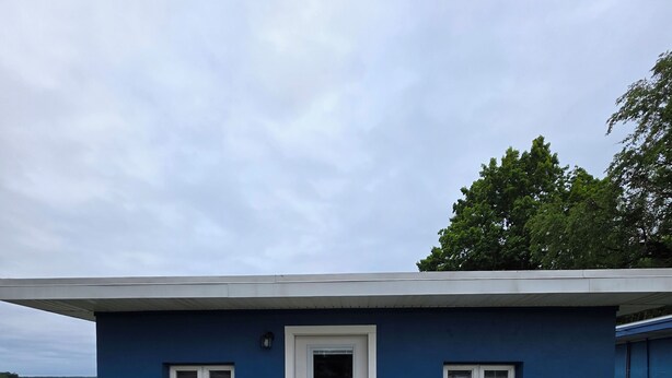 A blue house with a white door, two windows, a small porch, and a table. - Cozy 2-bedroom cottage in marvelous Ludington with AC (Ludington)