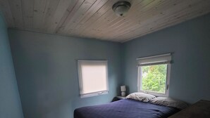 A bedroom with a bed, two windows, a ceiling light, and a wooden desk. - Cozy 2-bedroom cottage in marvelous Ludington with AC (Ludington)