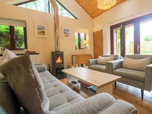 A living room with a sofa, armchairs, a coffee table, a fireplace, and a window with a view of greenery. - The Lodge at Lamburn (Truro)