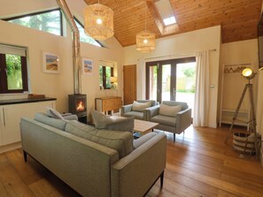 Ein gemütliches Wohnzimmer mit einer Couch, Sesseln, Holzboden, Kamin und einem großen Fenster.