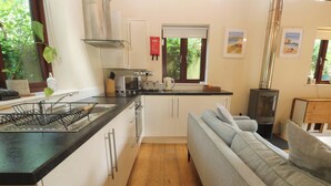 A compact kitchen with a stove, sink, and a window overlooking greenery. - The Lodge at Lamburn (Truro)