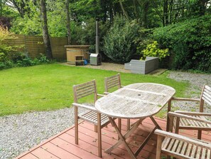 Eine Holzterrasse mit Tisch und Stühlen, umgeben von einem Rasen und dichter Bepflanzung.